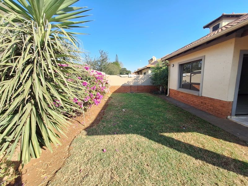 A private rear garden area featuring a lawn, established landscaping, and a brick boundary wall, adjacent to the townhouse structure.