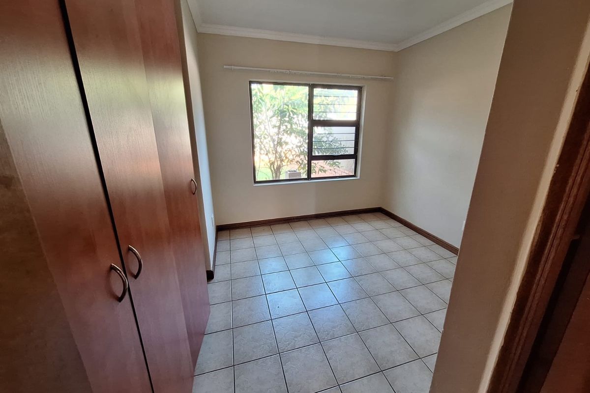 A vacant bedroom featuring tiled flooring, built-in wooden cupboards, and a window fitted with security bars.