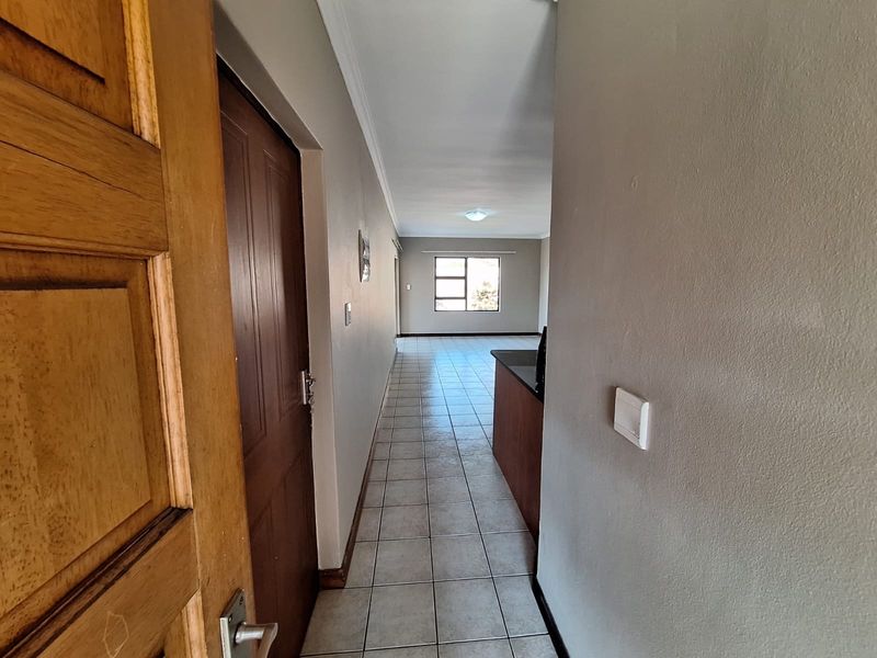 An entrance hallway with tiled flooring leading into an open-plan living area, featuring neutral wall tones and a view towards the rear window.