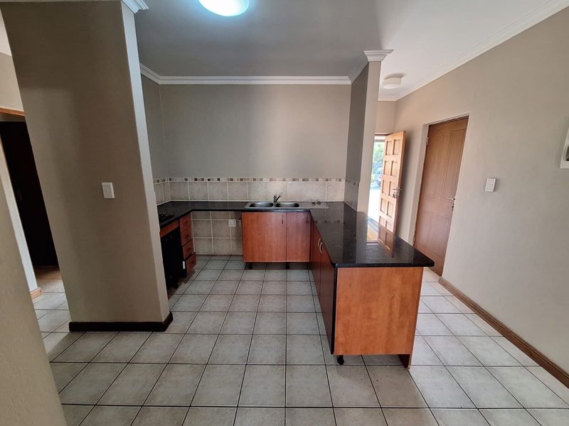 A functional kitchen featuring L-shaped wooden cabinetry, dark granite countertops, a double bowl sink, and neutral ceramic floor tiles.