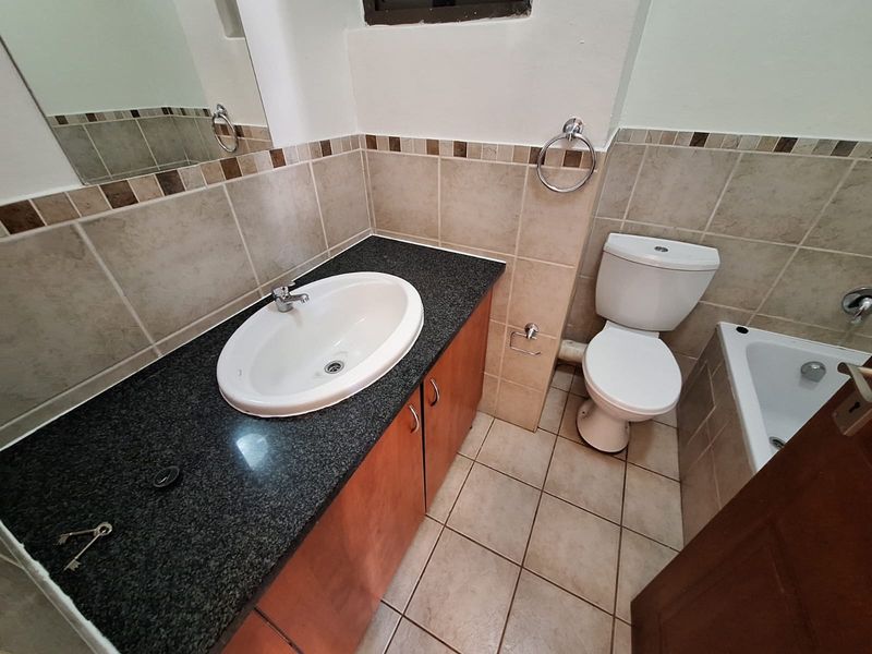 A functional bathroom featuring a vanity with granite countertop, drop-in basin, toilet, and a bathtub with neutral wall and floor tiling.
