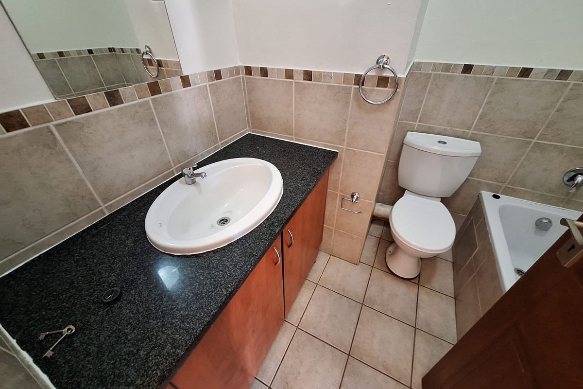 A functional bathroom featuring a vanity with granite countertop, drop-in basin, toilet, and a bathtub with neutral wall and floor tiling.