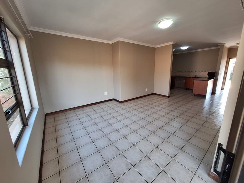 An open-plan living and kitchen area featuring neutral tiled flooring, built-in cabinetry with granite countertops, and ample natural light from large windows.