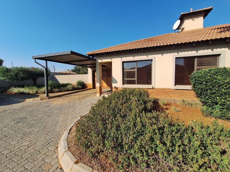 Front elevation of a townhouse featuring a tiled roof, brick accents, a paved driveway, and a covered carport area.