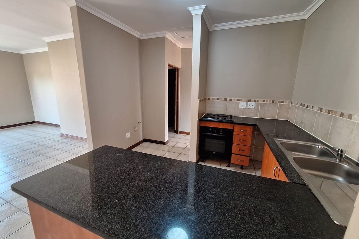A functional kitchen featuring granite countertops, built-in oven and hob, double sink, and tiled flooring, flowing into an open-plan living area.