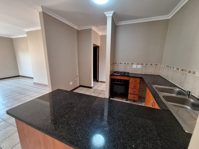 A functional kitchen featuring granite countertops, built-in oven and hob, double sink, and tiled flooring, flowing into an open-plan living area.