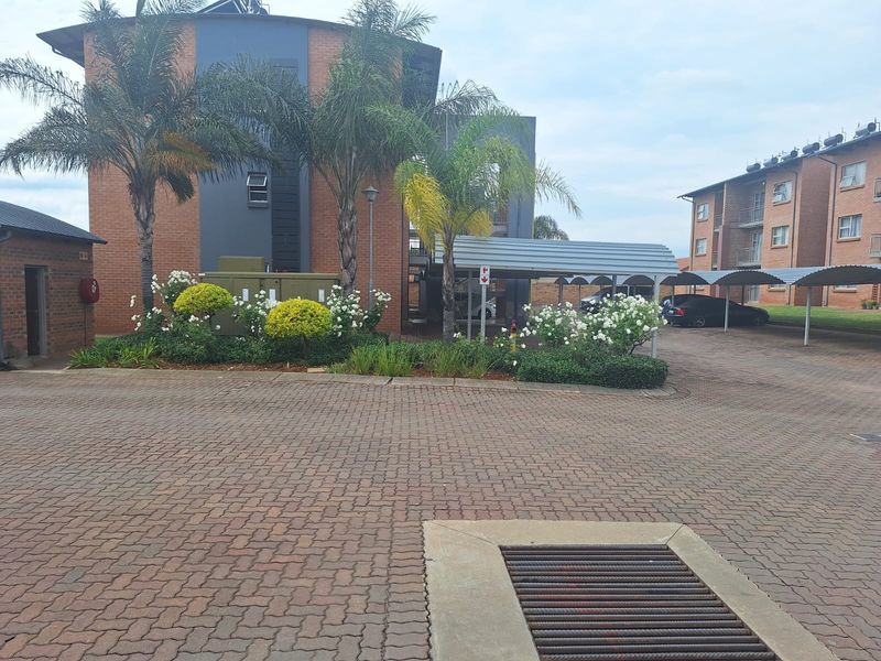 Exterior view of the apartment complex featuring a paved driveway, covered carport parking, and established garden landscaping.