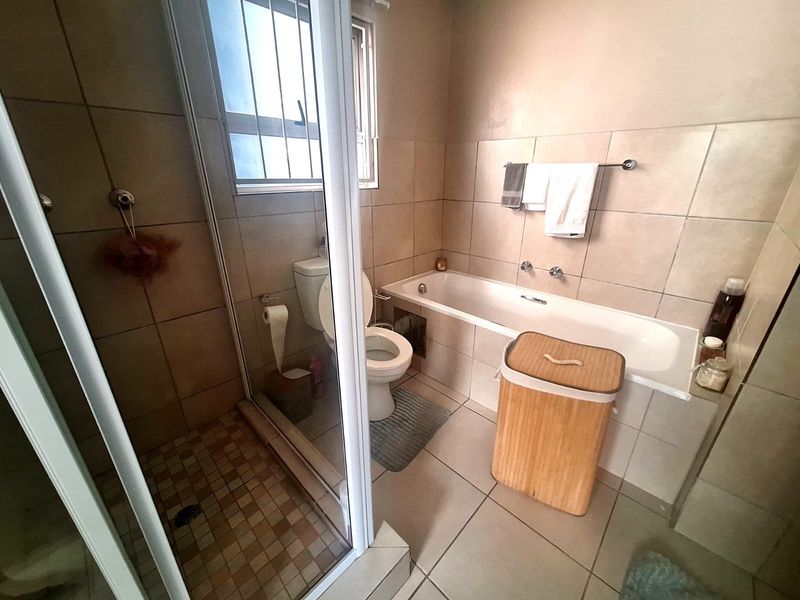 A functional bathroom featuring a separate shower enclosure, bathtub, toilet, and neutral wall and floor tiling.