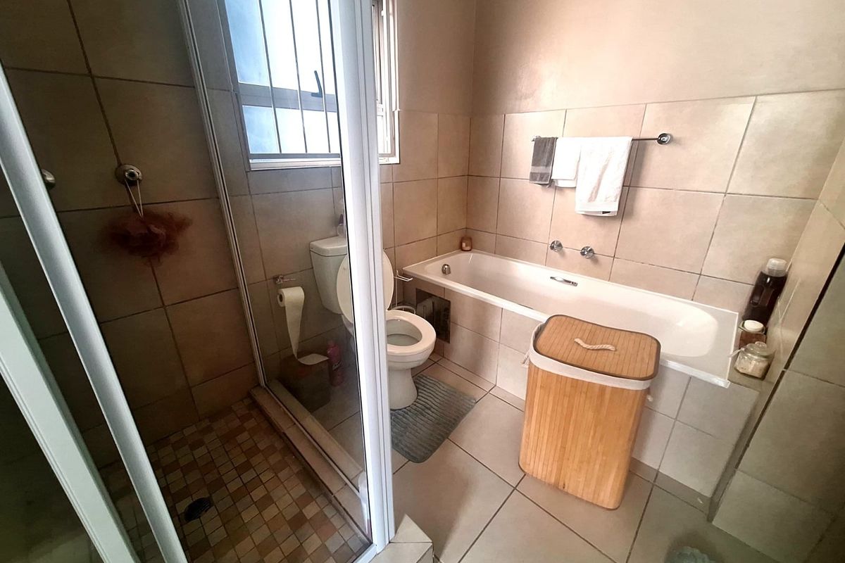 A functional bathroom featuring a separate shower enclosure, bathtub, toilet, and neutral wall and floor tiling.