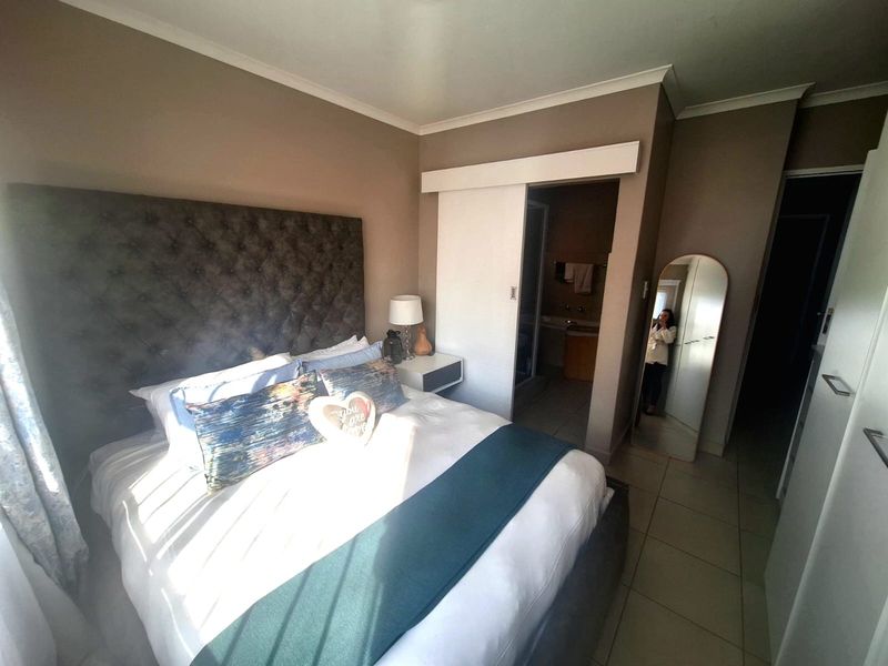 A well-maintained bedroom featuring tiled flooring, neutral wall tones, and direct access to an en-suite bathroom via a sliding door.