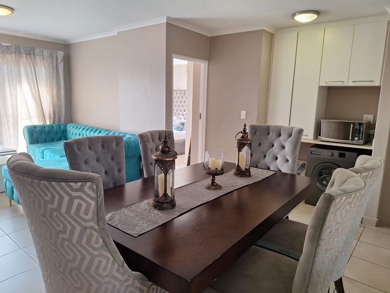 An open-plan dining and living area featuring tiled flooring, neutral wall tones, and built-in cabinetry with integrated laundry appliance space.