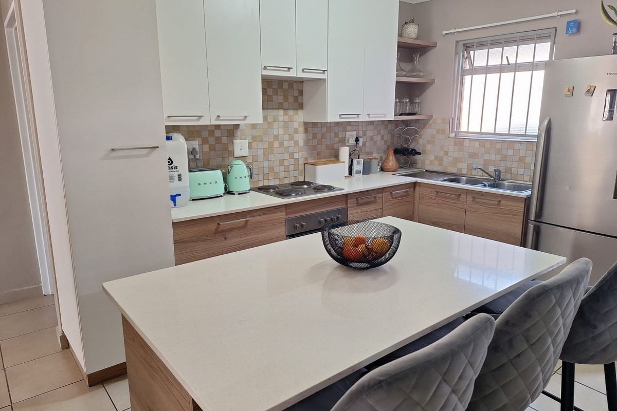 Modern kitchen featuring a central island with stone countertop, ample built-in cabinetry, mosaic tile backsplash, and integrated stainless steel appliances.