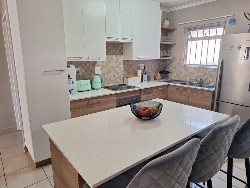 Modern kitchen featuring a central island with stone countertop, ample built-in cabinetry, mosaic tile backsplash, and integrated stainless steel appliances.
