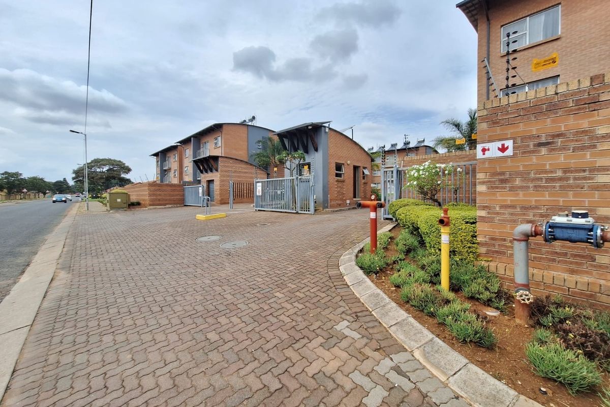 View of the apartment complex entrance featuring brick paving, secure gated access, electric fencing, and exterior fire safety infrastructure.