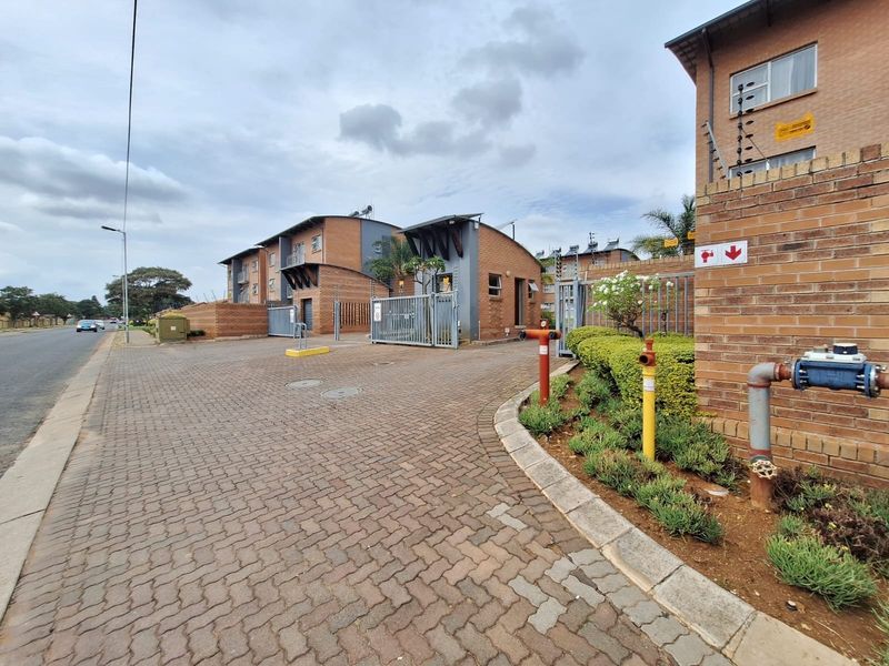 View of the apartment complex entrance featuring brick paving, secure gated access, electric fencing, and exterior fire safety infrastructure.