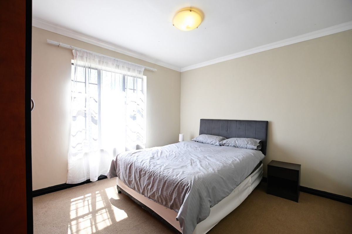 A functional bedroom featuring carpeted flooring, built-in cupboards, and security bars on the window, providing a neutral space ready for personalization.