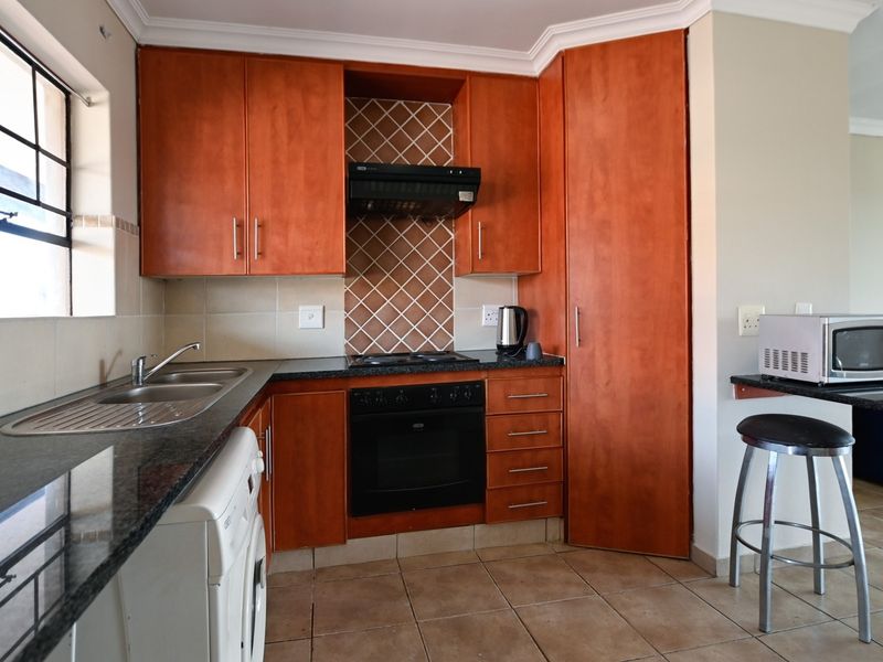 Functional kitchen featuring warm-toned wooden cabinetry, granite countertops, built-in oven, hob, extractor fan, and tiled flooring with a practical layout.