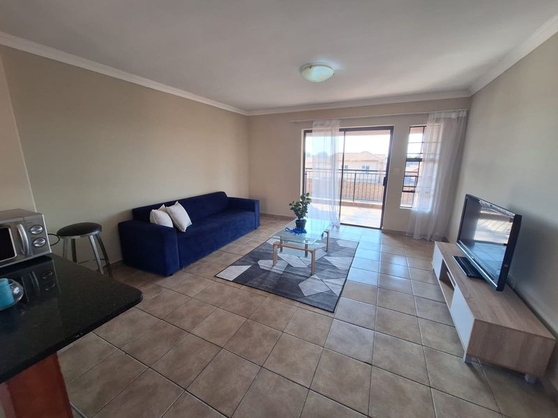 Open-plan living area featuring tiled flooring, a granite kitchen counter, and direct access to a private balcony through sliding glass doors.