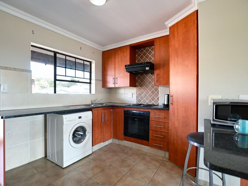 A functional kitchen featuring wood-finish cabinetry, granite countertops, built-in oven and hob, tiled backsplash, and space for a washing machine.