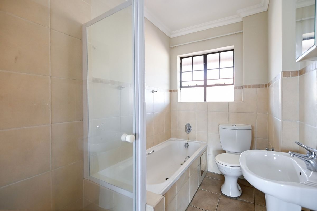 A functional bathroom featuring a bathtub with a glass shower screen, a pedestal basin, and a toilet, finished with neutral wall and floor tiles.