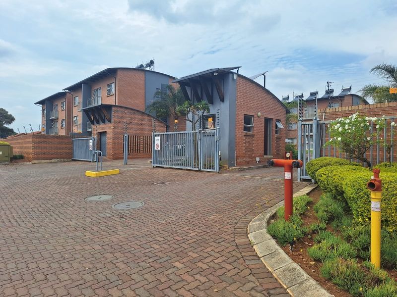 Front entrance view of the apartment complex featuring brick paving, secure gated access, and established landscaping.