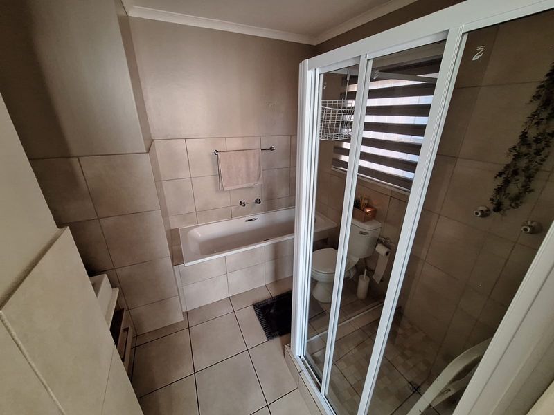 A functional bathroom featuring a built-in bathtub, a separate shower enclosure with sliding doors, and a toilet, finished with neutral wall and floor tiles.