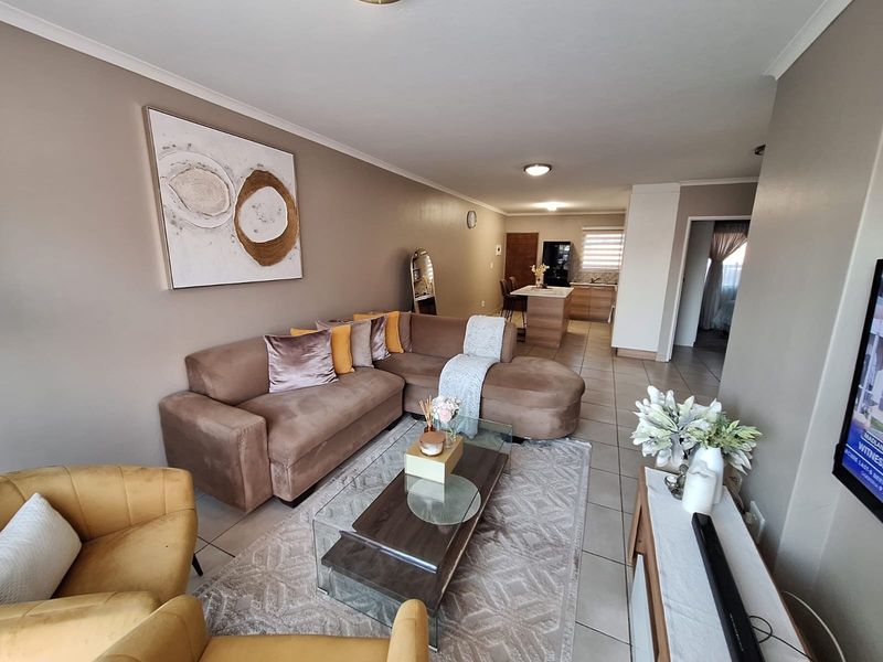 An open-plan living and kitchen area featuring neutral wall tones, tiled flooring, and a functional kitchen layout with a central island.