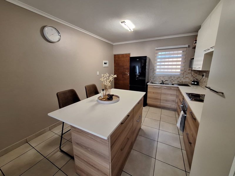 Modern kitchen featuring a central island, wood-finish cabinetry, tiled flooring, and integrated appliances, offering a functional and well-maintained cooking and dining space.