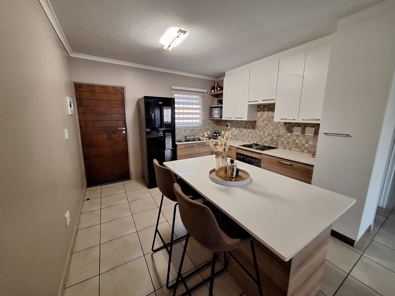 Modern kitchen featuring white and timber cabinetry, stone countertops, a central island, mosaic backsplash, and tiled flooring.