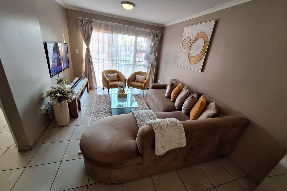 A well-maintained living room featuring neutral wall tones, tiled flooring, and a large sliding glass door that provides natural light.
