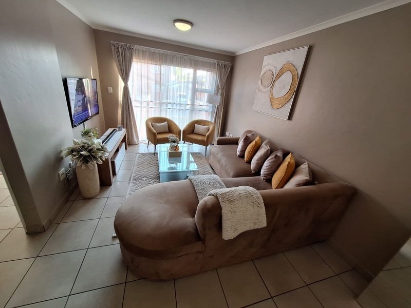 A well-maintained living room featuring neutral wall tones, tiled flooring, and a large sliding glass door that provides natural light.