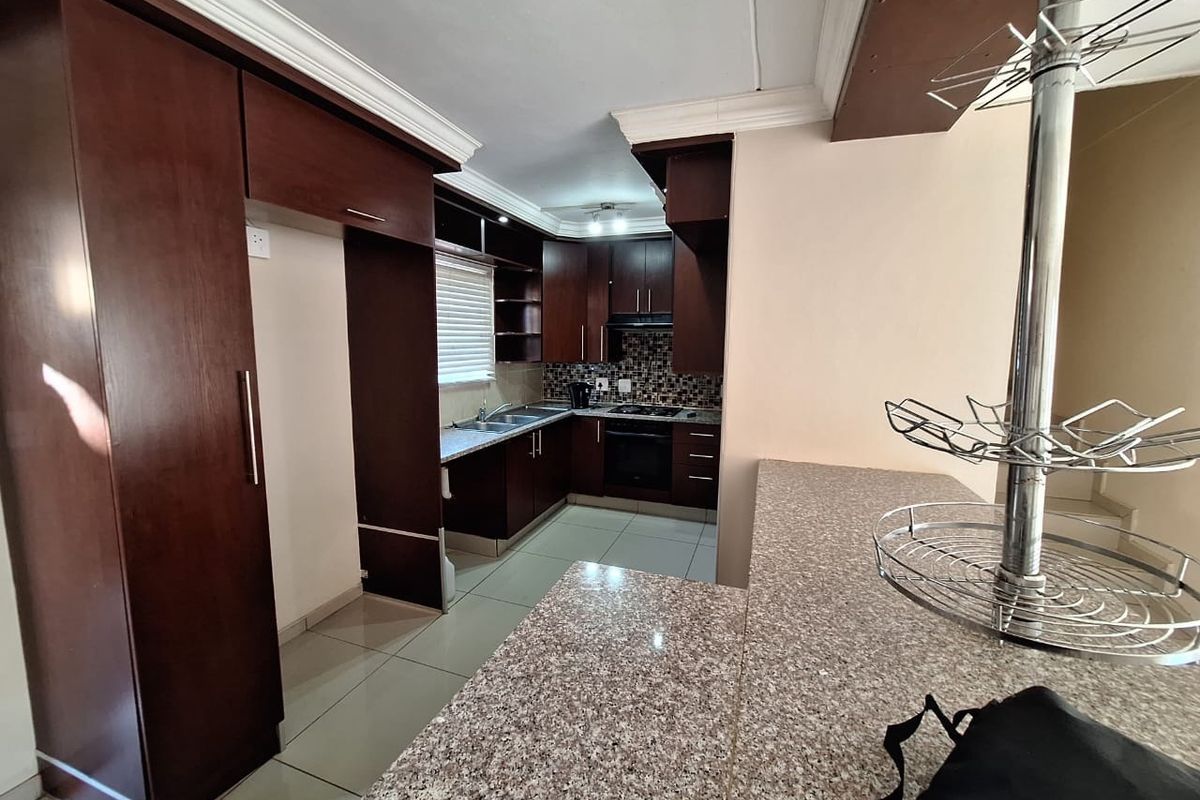 A functional kitchen featuring dark wood cabinetry, granite countertops, a breakfast bar, and built-in appliances including an oven and hob.