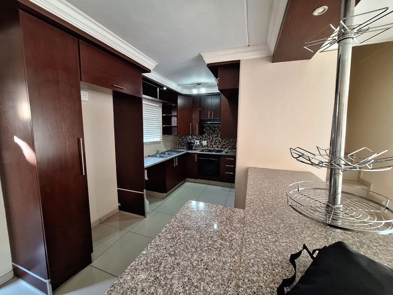 A functional kitchen featuring dark wood cabinetry, granite countertops, a breakfast bar, and built-in appliances including an oven and hob.