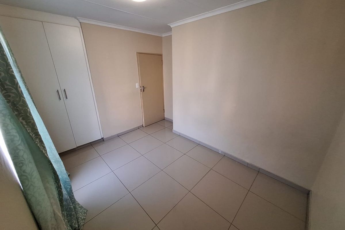 A clean, empty bedroom featuring neutral tiled flooring, a built-in wardrobe, and simple finishes, ready for personalization.