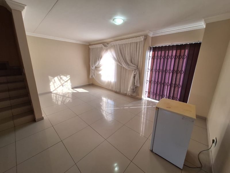 Spacious, light-filled living area featuring neutral tiled flooring, a staircase, and direct access to the exterior through a secure sliding door.