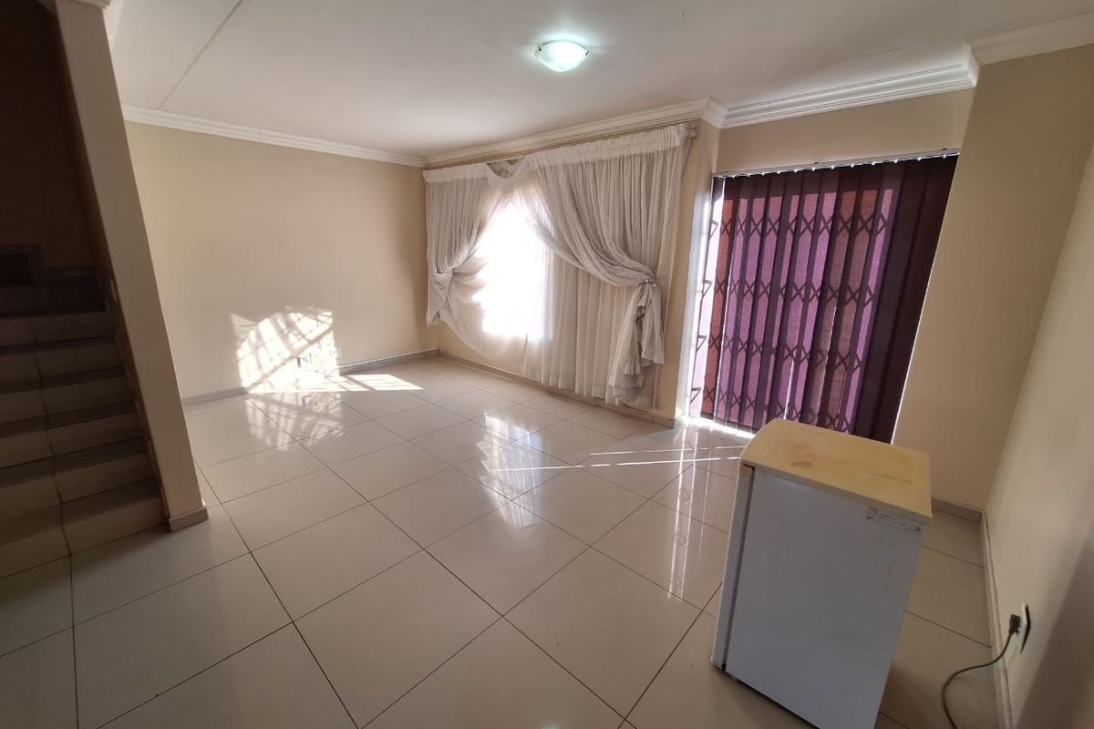 Spacious, light-filled living area featuring neutral tiled flooring, a staircase, and direct access to the exterior through a secure sliding door.