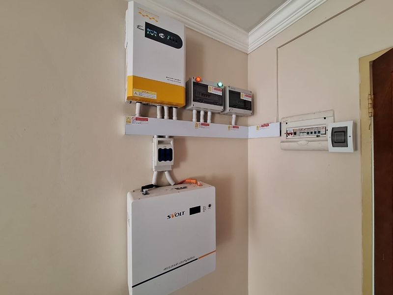 A wall-mounted solar power system featuring a hybrid inverter, lithium-ion battery storage, and an electrical distribution board.
