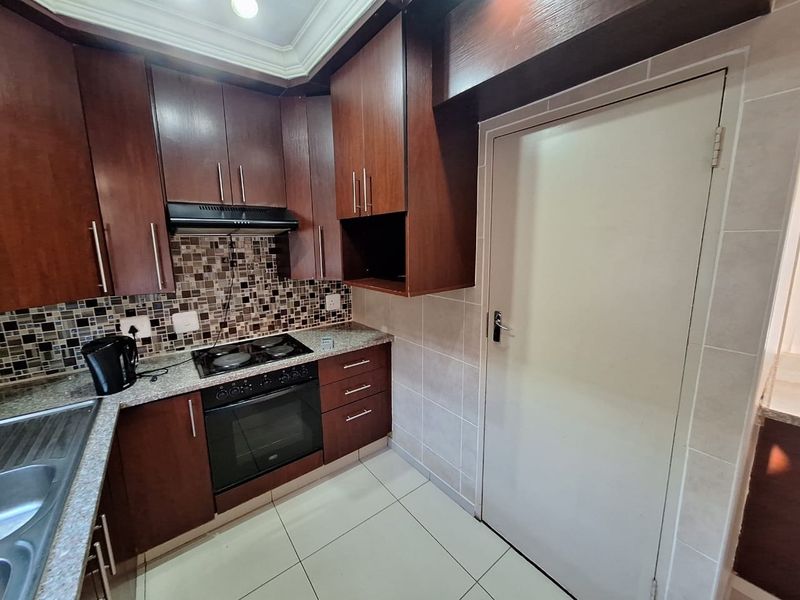A functional kitchen featuring dark wood cabinetry, granite countertops, a mosaic tile backsplash, and integrated appliances including an oven and hob.