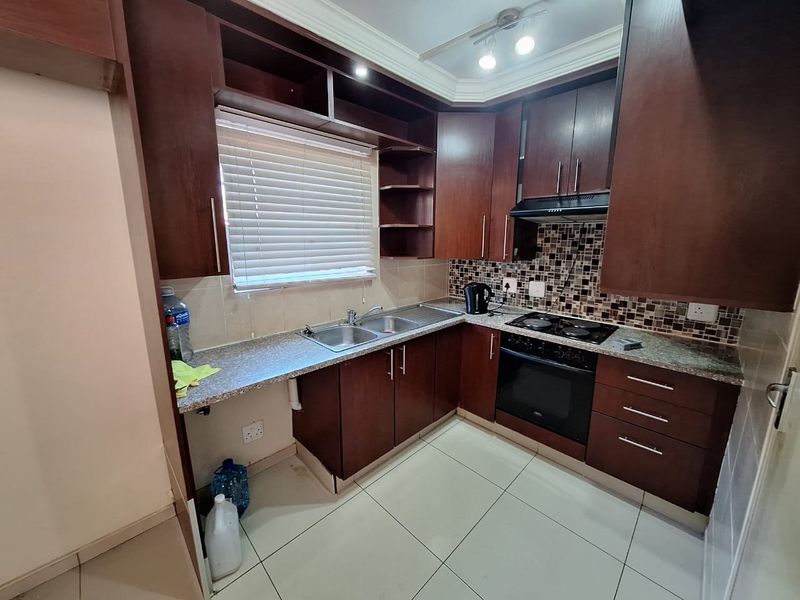 A functional kitchen featuring dark wood cabinetry, mosaic tile backsplash, built-in oven, electric hob, and tiled flooring with ample storage space.