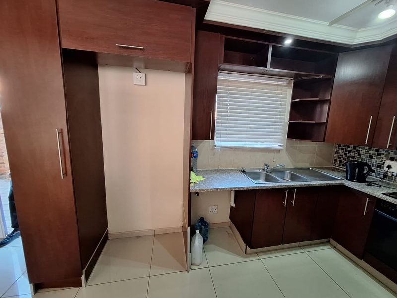 A functional kitchen featuring dark wood cabinetry, a double sink, tiled backsplash, and dedicated space for a refrigerator.