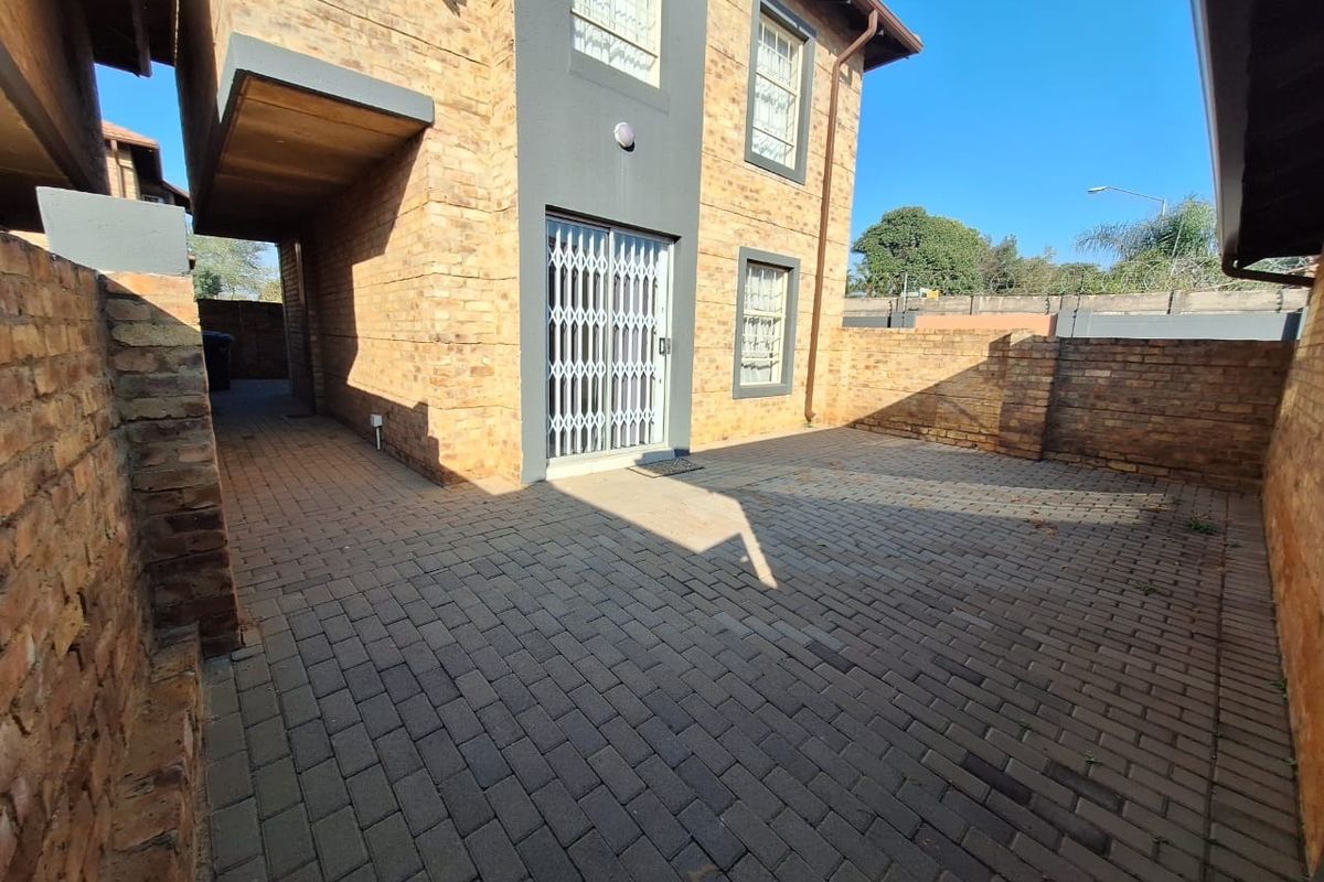 A private rear courtyard featuring brick paving, enclosed by a brick boundary wall, with access to the townhouse via a sliding door with security gate.