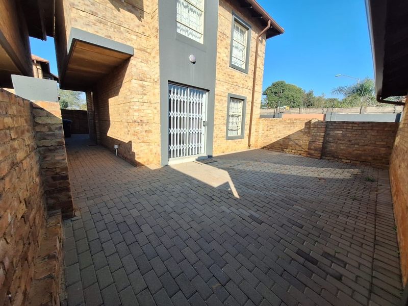 A private rear courtyard featuring brick paving, enclosed by a brick boundary wall, with access to the townhouse via a sliding door with security gate.