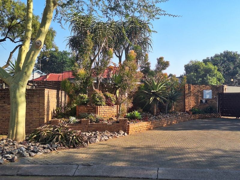 Front exterior view of the townhouse featuring a paved driveway, established garden with brick retaining walls, and secure boundary fencing.