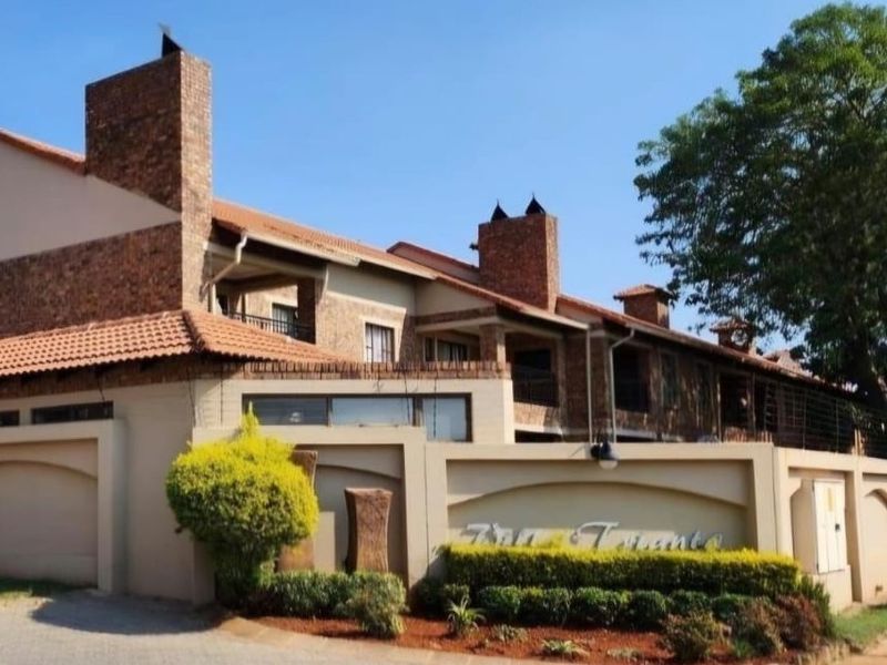 Front exterior view of a multi-unit townhouse complex featuring brick facades, tiled roofing, and secure boundary walling with established landscaping.