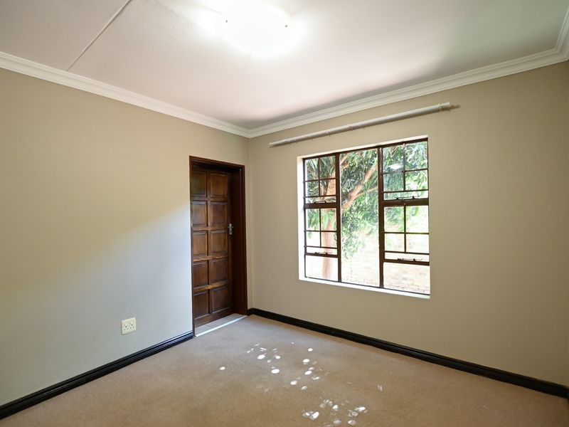 A vacant bedroom featuring neutral walls, carpeted flooring, a wooden door, and a window with security bars.