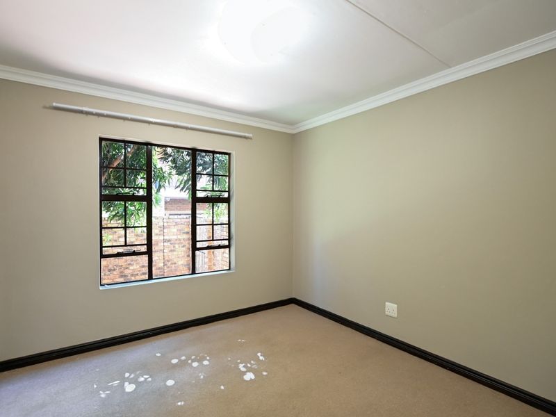 A vacant bedroom featuring neutral wall paint, dark skirting boards, and a steel-framed window overlooking the exterior.