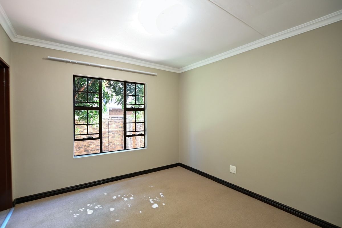 A vacant bedroom featuring neutral wall paint, dark skirting boards, and a steel-framed window overlooking the exterior.