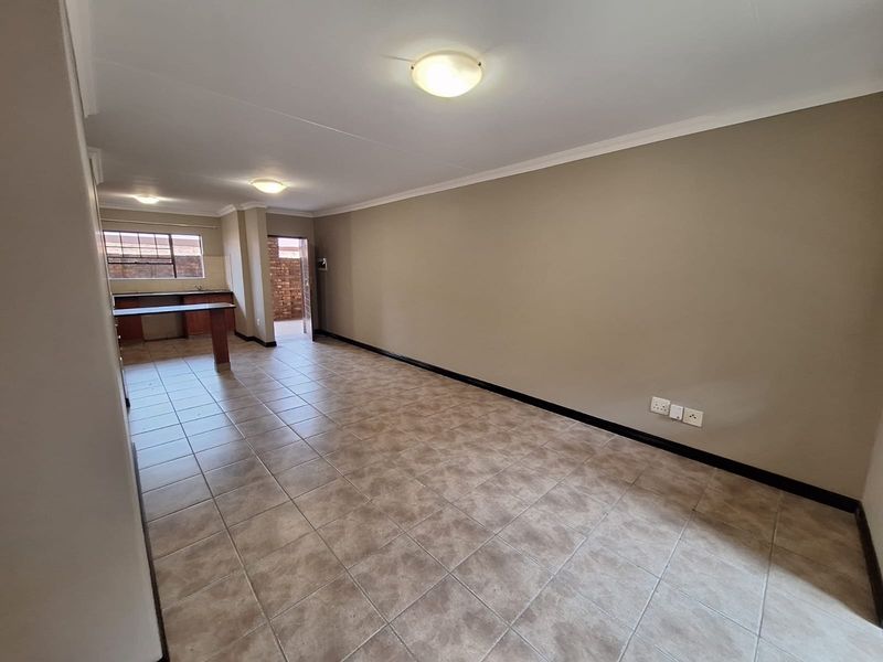 An open-plan living and kitchen area featuring tiled flooring, neutral walls, and a breakfast bar, offering a versatile space for living and dining.
