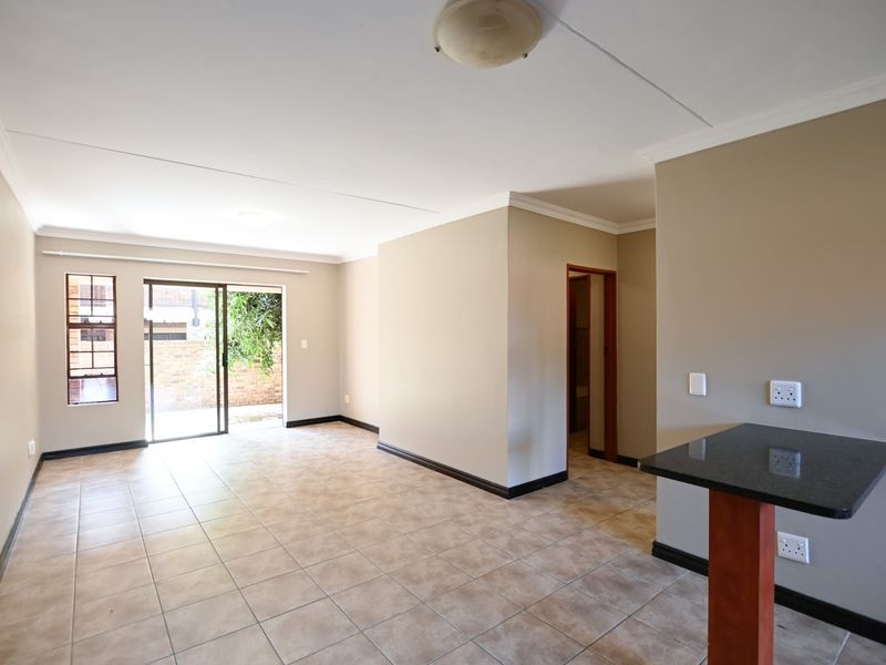 Spacious open-plan living area featuring neutral walls, tiled flooring, and a granite breakfast bar, with direct access to an outdoor patio area.