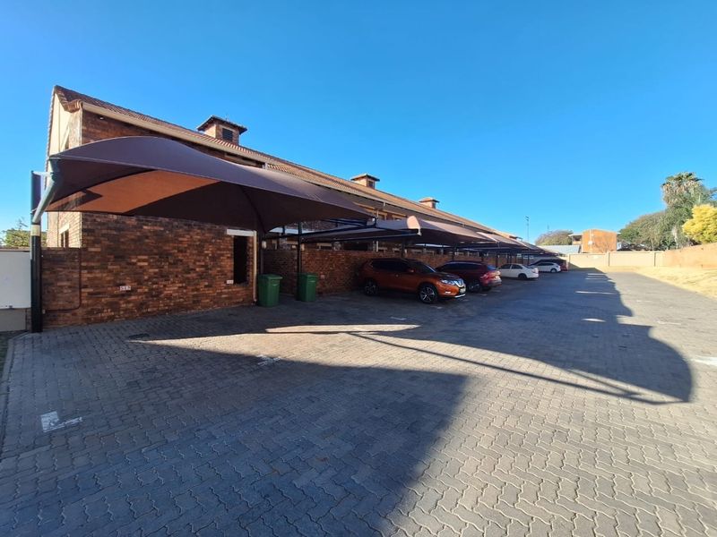 Exterior view of a townhouse complex featuring a paved parking area with covered shade cloth carports and face brick building facades.